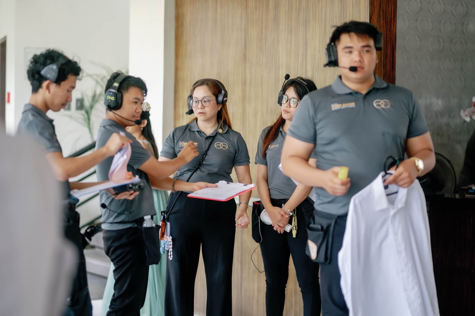Five coordinators in branded polos and headsets during preparations, one holding a run sheet on a clipboard